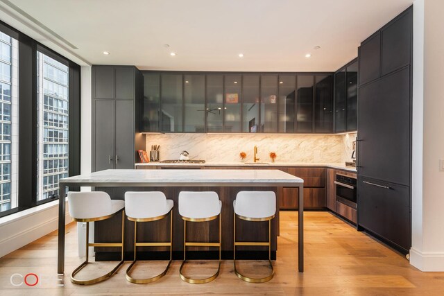 kitchen with light hardwood / wood-style flooring, tasteful backsplash, light stone countertops, a kitchen island, and oven