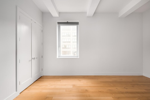 unfurnished bedroom featuring beamed ceiling, baseboards, and light wood-style flooring