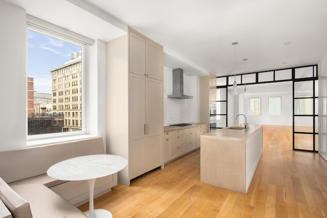 kitchen with wall chimney range hood, a sink, stainless steel gas stovetop, backsplash, and light wood-type flooring