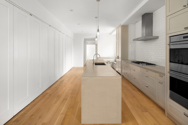 kitchen featuring stainless steel appliances, wall chimney exhaust hood, a sink, tasteful backsplash, and a center island with sink