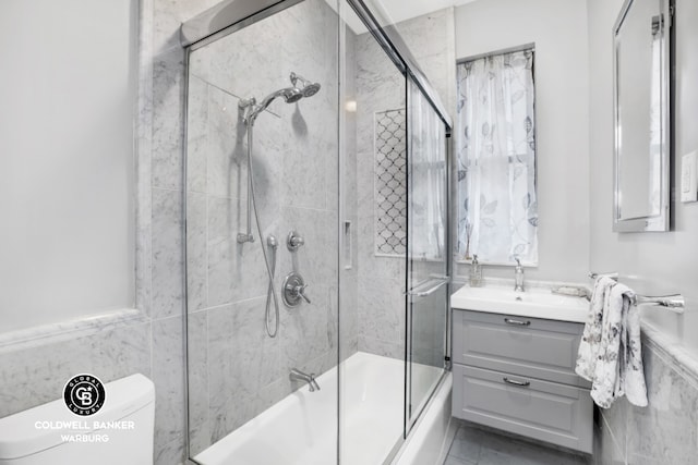 bathroom featuring toilet, combined bath / shower with glass door, vanity, and tile walls