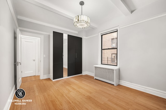 unfurnished bedroom featuring wood-type flooring, radiator heating unit, beam ceiling, and a closet