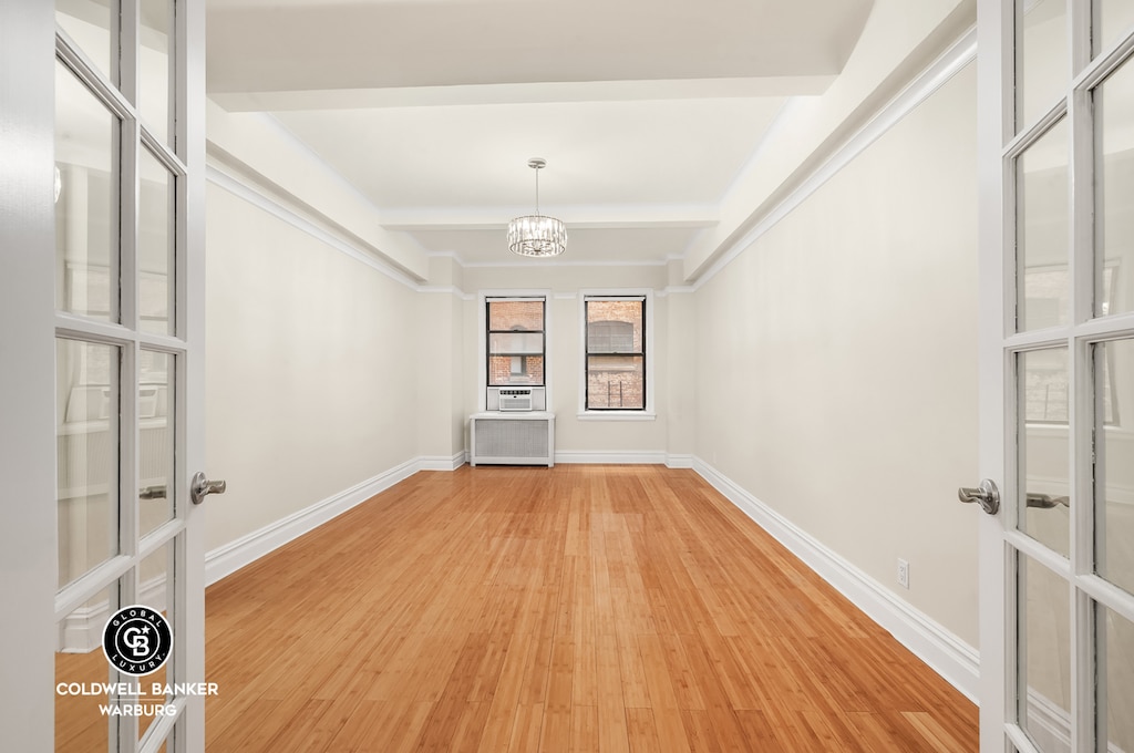 unfurnished dining area featuring light wood finished floors, a chandelier, baseboards, beam ceiling, and radiator