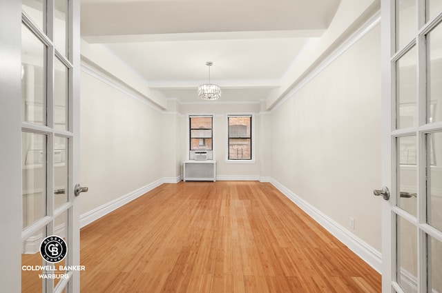 unfurnished dining area featuring light wood finished floors, a chandelier, baseboards, beam ceiling, and radiator
