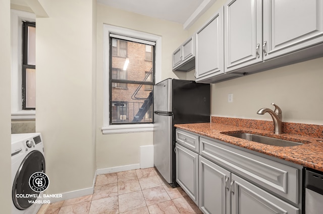 kitchen featuring stone counters, washer / clothes dryer, freestanding refrigerator, a sink, and baseboards