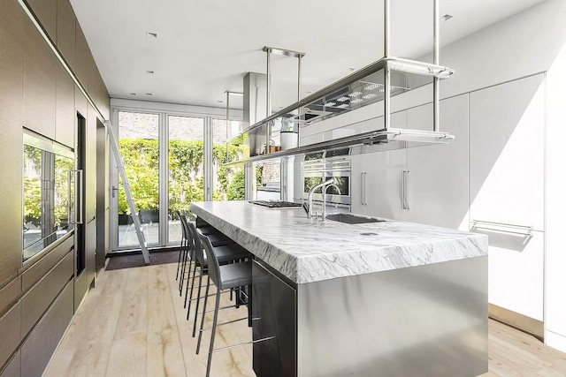 kitchen featuring a breakfast bar, a sink, light wood finished floors, modern cabinets, and a center island with sink