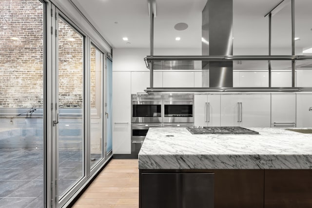 kitchen featuring light wood finished floors, white cabinets, modern cabinets, appliances with stainless steel finishes, and light stone counters