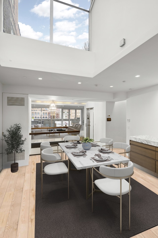 dining space with a towering ceiling, light wood-style floors, and recessed lighting