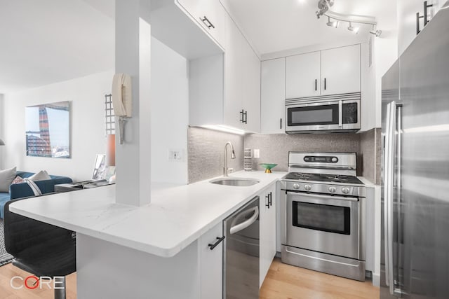 kitchen with backsplash, appliances with stainless steel finishes, light wood-style floors, white cabinetry, and a sink