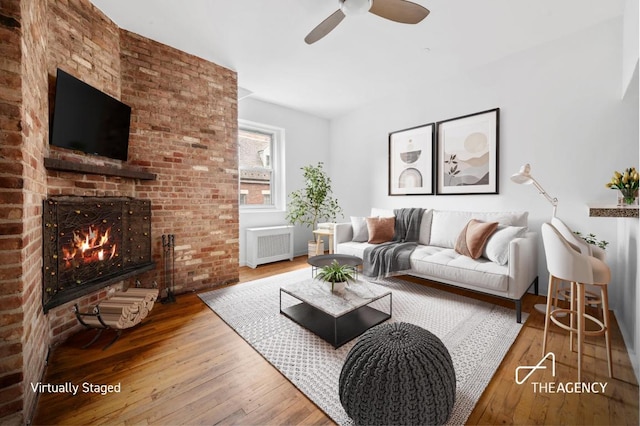 living room featuring ceiling fan, radiator, a brick fireplace, and hardwood / wood-style floors