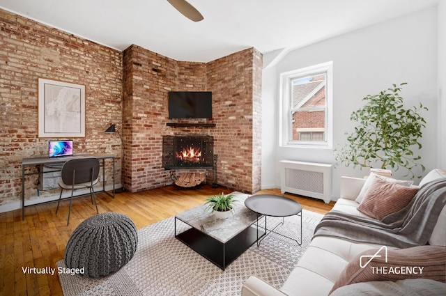 living room featuring brick wall, radiator heating unit, a brick fireplace, and wood-type flooring