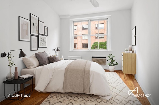 bedroom featuring hardwood / wood-style flooring, a wall mounted AC, and ceiling fan