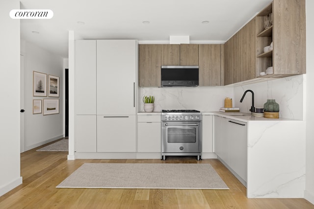 kitchen featuring tasteful backsplash, white cabinets, sink, and high end stainless steel range oven