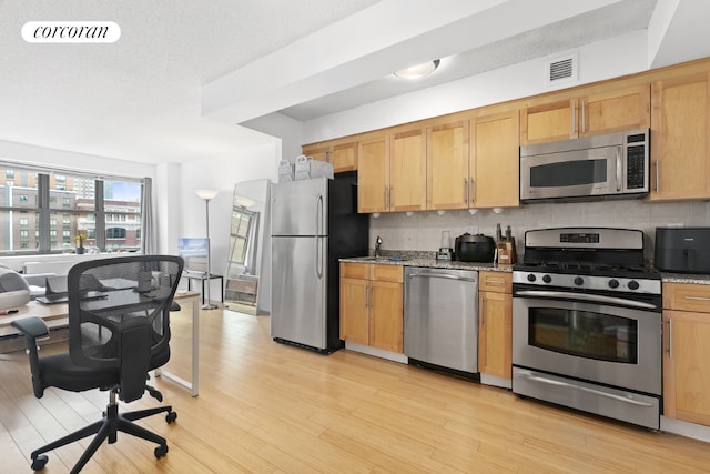 kitchen with appliances with stainless steel finishes, light wood-type flooring, backsplash, and light stone counters