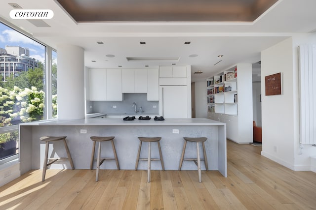 kitchen with white cabinets, modern cabinets, a breakfast bar area, white built in refrigerator, and light wood-type flooring