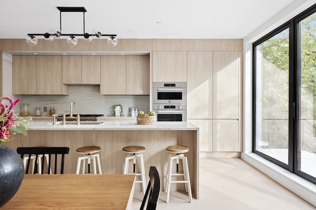 kitchen featuring stainless steel double oven, decorative light fixtures, sink, and light brown cabinets