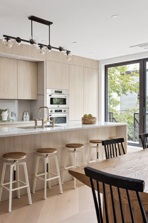 kitchen with light brown cabinetry, double oven, tasteful backsplash, and a kitchen bar