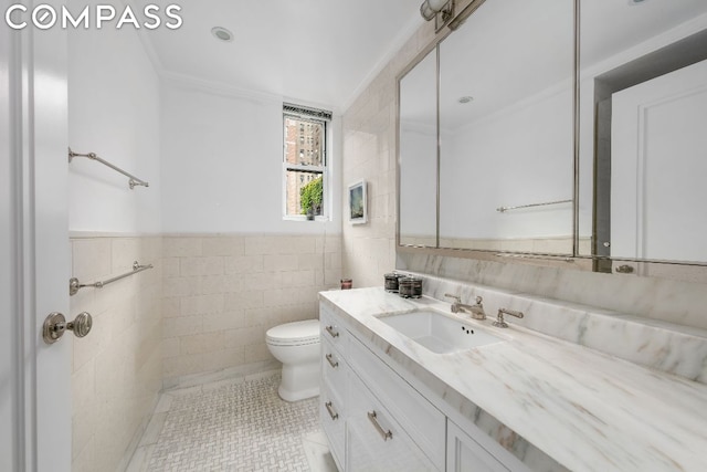 bathroom with toilet, tile patterned flooring, tile walls, ornamental molding, and vanity