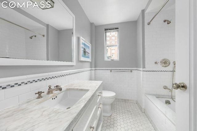 full bathroom featuring toilet, tiled shower / bath, tile patterned flooring, tile walls, and vanity