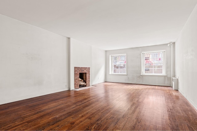 unfurnished living room featuring baseboards, radiator, a brick fireplace, and wood finished floors