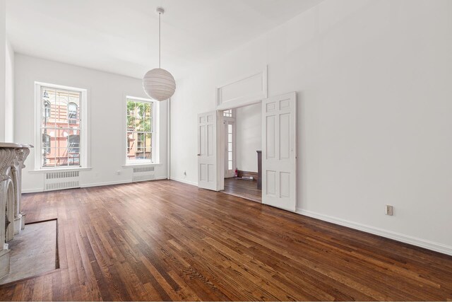 unfurnished living room with radiator, dark wood finished floors, and baseboards