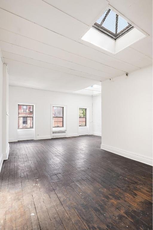 empty room featuring radiator, dark hardwood / wood-style flooring, and a skylight