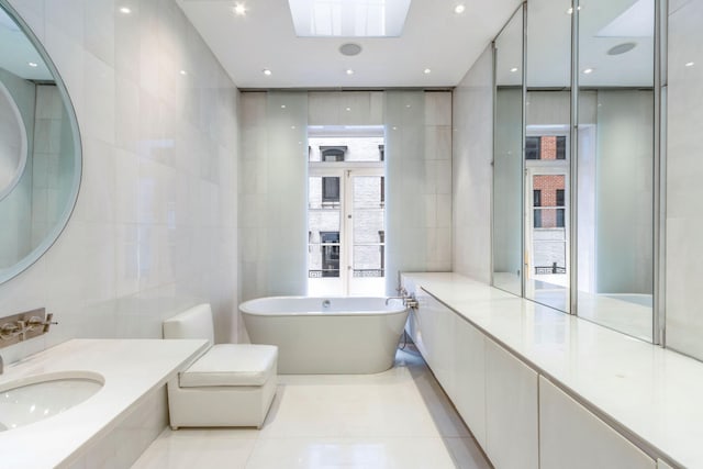 bathroom with a skylight, a sink, tile walls, a soaking tub, and tile patterned floors