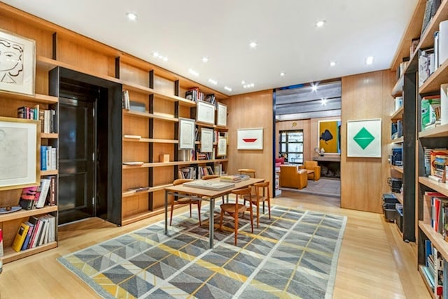 office with wall of books, wood walls, wood finished floors, and recessed lighting