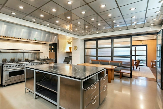 kitchen with dark countertops, a center island, luxury range, concrete flooring, and backsplash