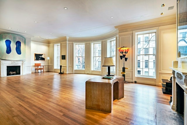 interior space featuring ornamental molding, a fireplace with flush hearth, light wood-style flooring, and a decorative wall