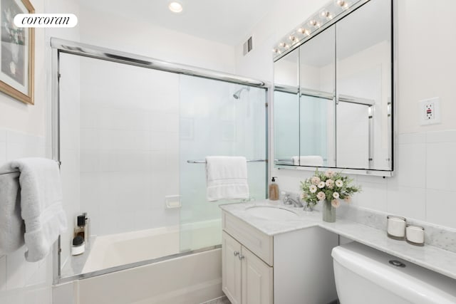 full bathroom with tile walls, combined bath / shower with glass door, vanity, and toilet