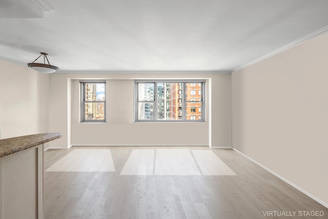 empty room featuring light wood-style flooring, ornamental molding, and baseboards
