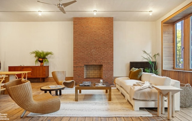 living area with ceiling fan, wood-type flooring, and a brick fireplace