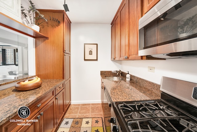 kitchen with stone counters, stainless steel appliances, a sink, baseboards, and brown cabinetry