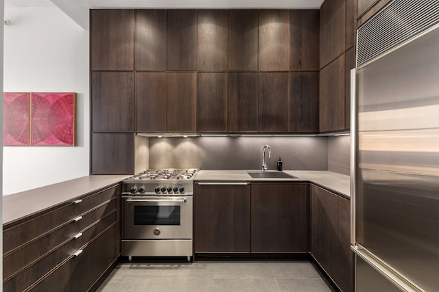 kitchen featuring dark brown cabinetry, sink, light tile patterned flooring, and appliances with stainless steel finishes