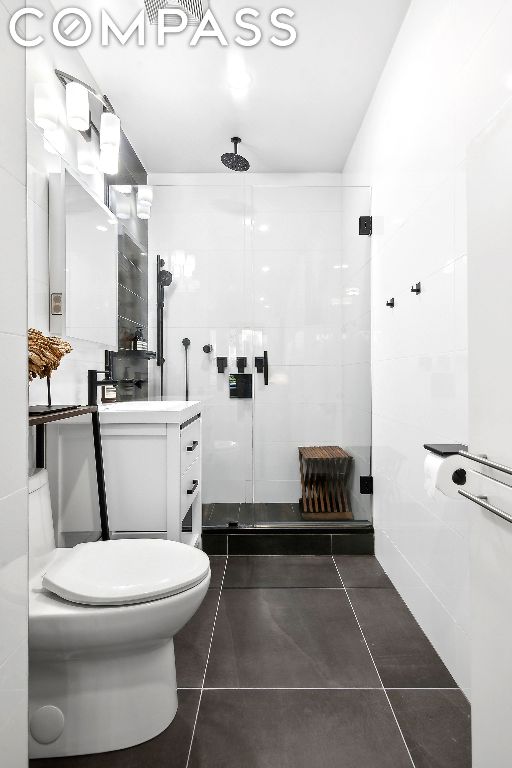 bathroom featuring tile patterned flooring, vanity, tile walls, and a shower with shower door