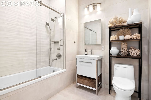 full bathroom featuring toilet, vanity, tile walls, and combined bath / shower with glass door