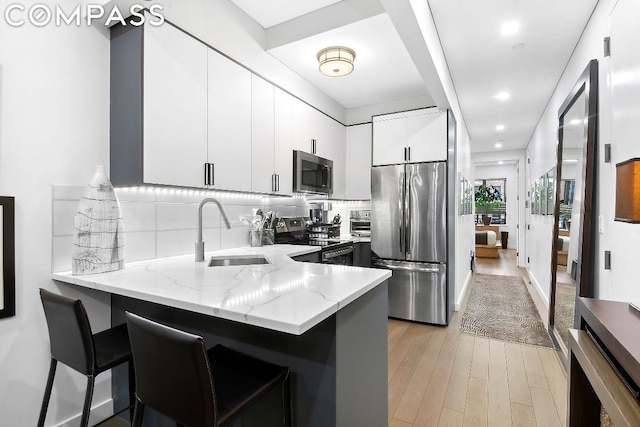 kitchen with white cabinets, appliances with stainless steel finishes, sink, kitchen peninsula, and a breakfast bar area