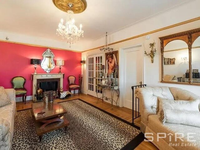 living room with a brick fireplace, hardwood / wood-style floors, an inviting chandelier, and french doors