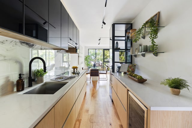 kitchen with sink, rail lighting, light stone countertops, beverage cooler, and light wood-type flooring