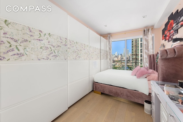 bedroom with a city view, light wood-style floors, and a wainscoted wall