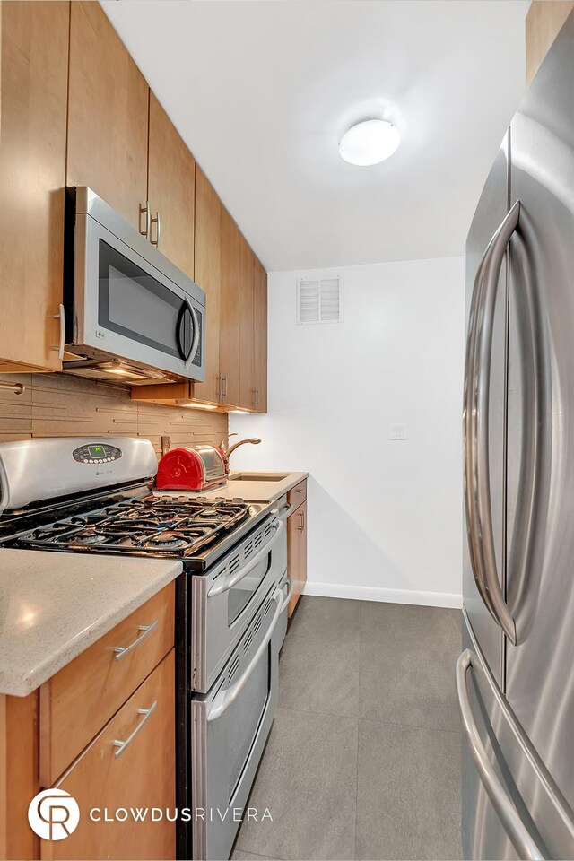 kitchen with appliances with stainless steel finishes, tasteful backsplash, light stone counters, and sink