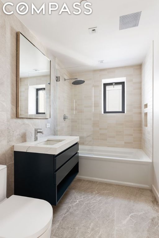 full bathroom featuring toilet, tiled shower / bath combo, tile walls, and vanity