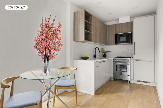 kitchen with backsplash, high end range, sink, white cabinetry, and light hardwood / wood-style flooring