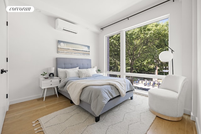 bedroom with a wall mounted AC and light hardwood / wood-style flooring