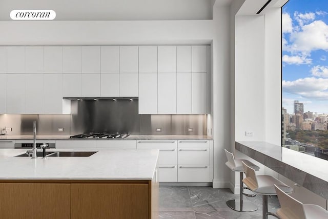 kitchen with white cabinets, stainless steel gas stovetop, tasteful backsplash, and a healthy amount of sunlight