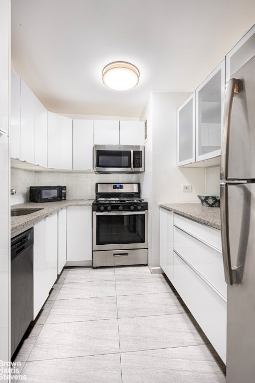 kitchen featuring light stone counters, white cabinetry, appliances with stainless steel finishes, and light tile patterned flooring