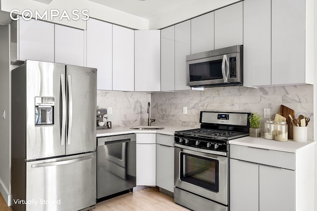 kitchen featuring a sink, backsplash, appliances with stainless steel finishes, white cabinets, and light countertops