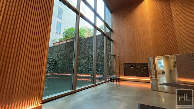 interior space featuring a towering ceiling, mail area, wooden walls, a wall of windows, and concrete floors