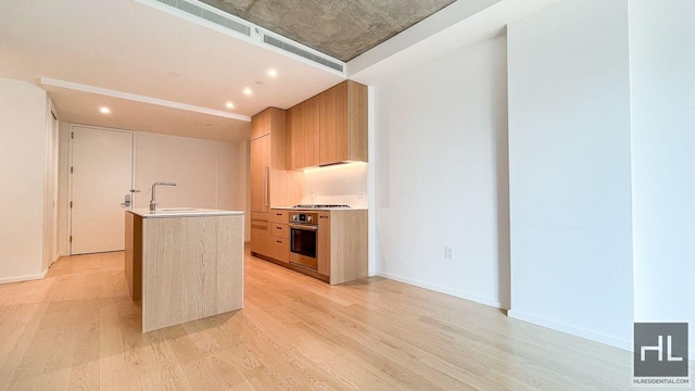 kitchen with stainless steel appliances, a kitchen island with sink, a sink, modern cabinets, and light wood-type flooring